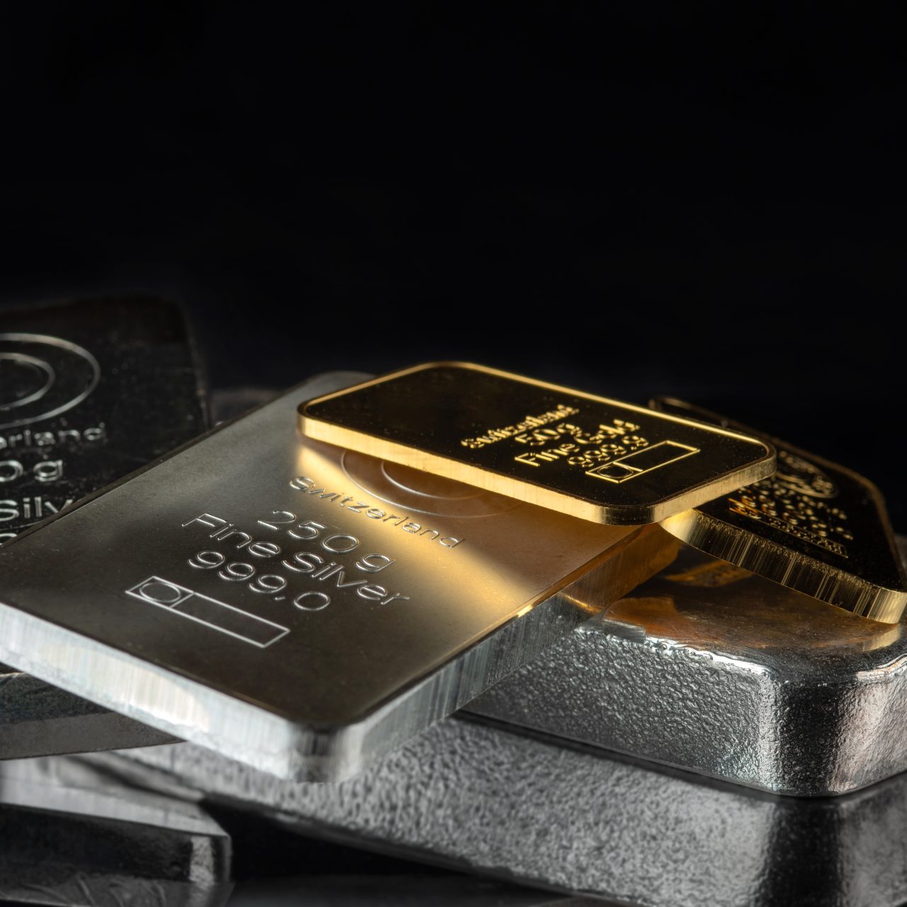Gold and silver bars of various weights on a dark background. Selective focus.