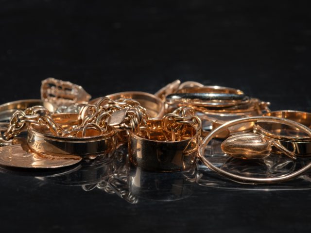 A bunch of different gold jewelry on a mirror black background. Selective focus.